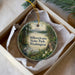 A decorative ornament in a box, featuring a scenic landscape with a mountain, trees, and a body of water.