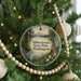 A round ornament hanging on a Christmas tree, featuring a scenic landscape with a lake, mountains, and trees.