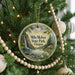 A round ornament hanging on a Christmas tree, featuring a scenic landscape with a waterfall and a cabin in the distance.