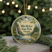 A round ornament with a scenic landscape of a waterfall, pine trees, and a house, hanging on a string.
