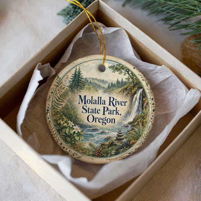 A decorative ornament in a box, featuring a scenic landscape with a waterfall and forest.