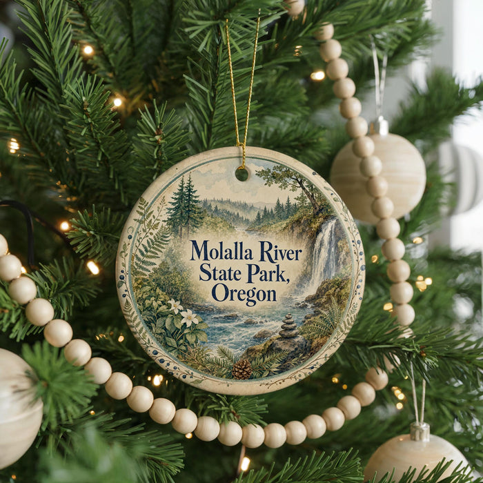 A round ornament hanging on a Christmas tree, featuring a scenic landscape with a river, mountains, and trees.
