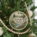 A round ornament hanging on a Christmas tree, featuring a scenic landscape with a river, mountains, and trees.