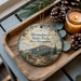 A decorative ornament featuring Monadnock State Park in New Hampshire, with pine cones and a lit candle on a wooden tray.