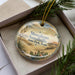 A decorative ornament in a box, featuring a desert landscape with cacti and a clear sky.
