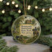 A round ornament with a painting of a historical scene, featuring a person on horseback, a cannon, and a building, surrounded by greenery.