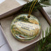 A decorative ornament in a box, featuring a scenic landscape with a lake, mountains, and a bird, along with the text "M Mormon Island State Recreation Area, Nebraska".