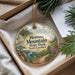 A decorative ornament with a scenic mountain landscape, featuring a bird perched on a tree branch, is displayed in a box with pine branches.