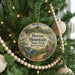A round ornament hanging on a Christmas tree, featuring a scenic landscape with mountains, trees, and a winding path.