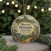 A round ornament with a scenic mountain landscape and a bird perched on a branch, hanging from a string.