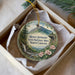 A decorative ornament in a box, featuring a mountain landscape with a waterfall and flowers.