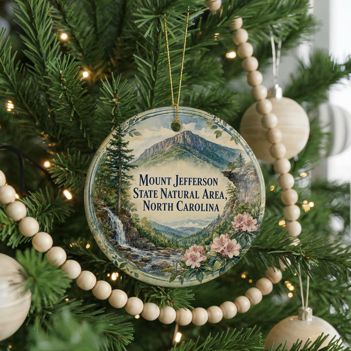 A round ornament hanging on a Christmas tree, featuring a scenic mountain landscape with a waterfall and flowers.