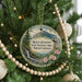 A round ornament hanging on a Christmas tree, featuring a scenic mountain landscape with a waterfall and flowers.