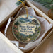 A decorative ornament in a box, featuring a scenic landscape with mountains, pine trees, and a castle-like structure.