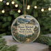 A round ornament with a scenic mountain landscape and a cabin in the background, hanging from a string.