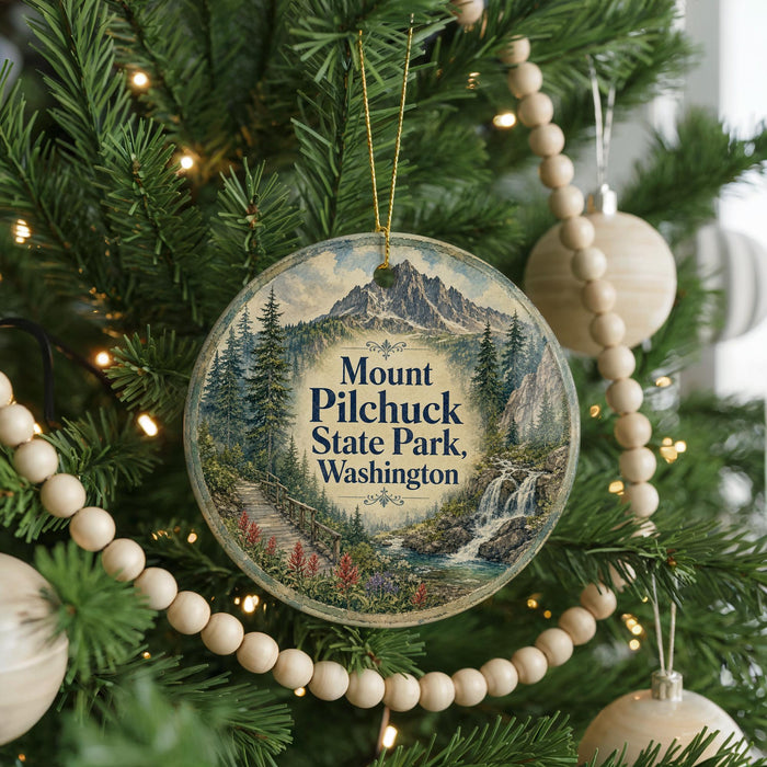 A round ornament hanging on a Christmas tree, featuring a scenic mountain landscape with a waterfall and pine trees.