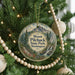 A round ornament hanging on a Christmas tree, featuring a scenic mountain landscape with a waterfall and pine trees.