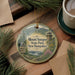 A decorative ornament featuring a scenic mountain landscape with a lighthouse, surrounded by pine branches and a cup of coffee on a wooden surface.