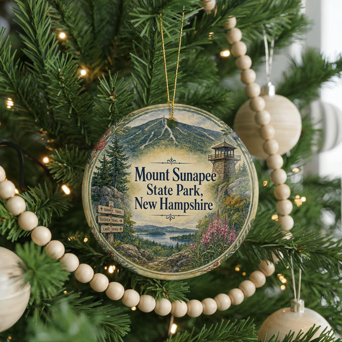 A round ornament hanging on a Christmas tree, featuring a scenic image of Mount Sunapee State Park in New Hampshire.