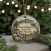 A round ornament with a scenic mountain landscape and a train, hanging on a string.