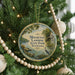 A round ornament hanging on a Christmas tree, featuring a scenic image of a lake and mountains with a bird in the foreground.