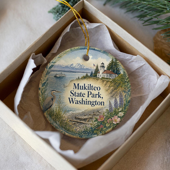 A decorative ornament in a box, featuring a scenic image of Mukilteo State Park in Washington with a lighthouse and a bird.