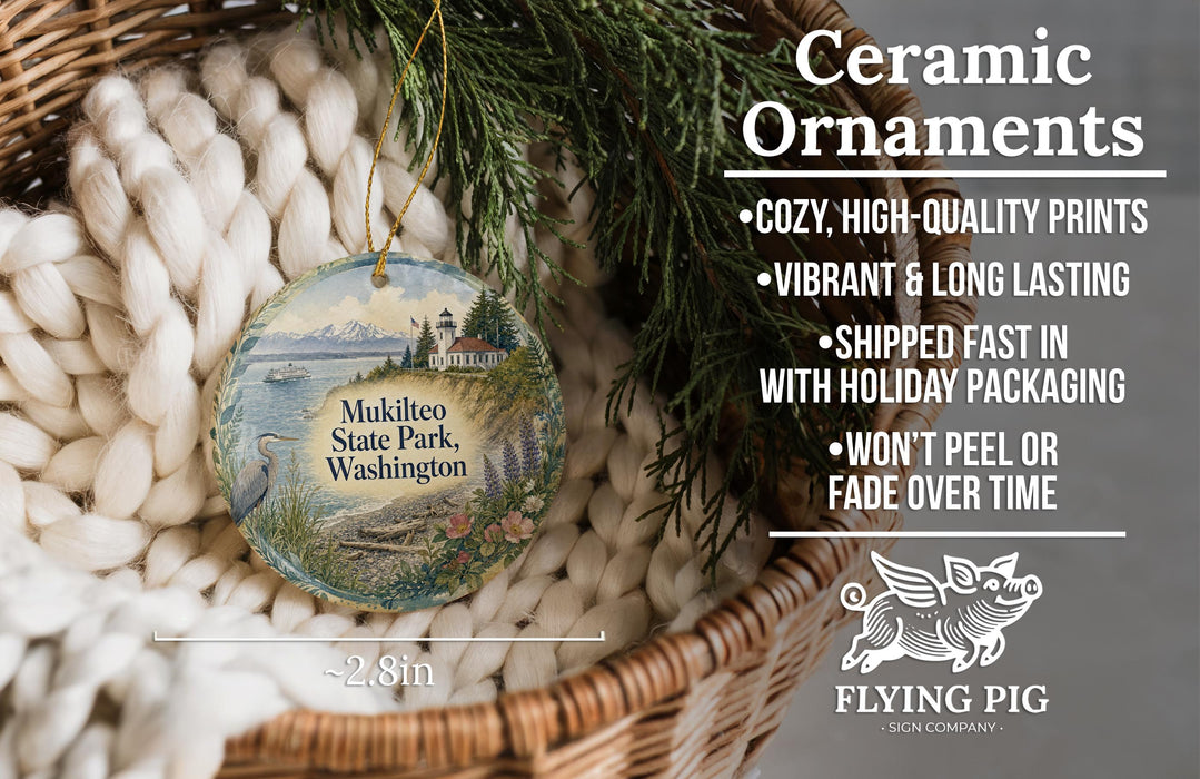 Ceramic ornaments, featuring a detailed image of Mukilteo State Park, Washington, are displayed in a woven basket. The ornaments are described as cozy, high-quality prints, vibrant, and long-lasting, and are shipped fast in holiday packaging. They are not to be peeled or faded over time. The image also includes a scale for size comparison and a logo for the Flying Pig Sign Company.