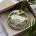 A round ornament with a scenic landscape of Mystery Bay State Park, Washington, featuring pine trees and a body of water.