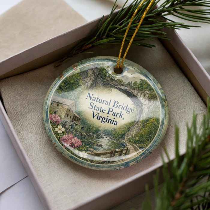 A decorative ornament in a box, featuring a scenic landscape with a river, bridge, and trees.