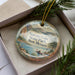 A decorative ornament in a box, featuring a scenic landscape with mountains, water, and a person in a canoe.