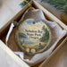 A decorative ornament in a white box, featuring a scenic landscape with a lake, mountains, and wildlife.