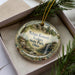 A decorative ornament with a scenic landscape of Nelson-Kennedy Lidges State Park, Ohio, displayed in a box with pine branches.