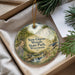 A decorative ornament with a scenic landscape of New Glarus Woods State Park, Wisconsin, featuring a winding path, a waterfall, and various plants and wildlife.