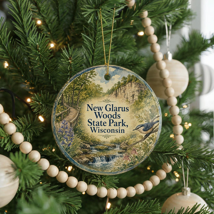 A round ornament hanging on a Christmas tree, featuring a scenic landscape with a river, waterfall, and a bird in flight.