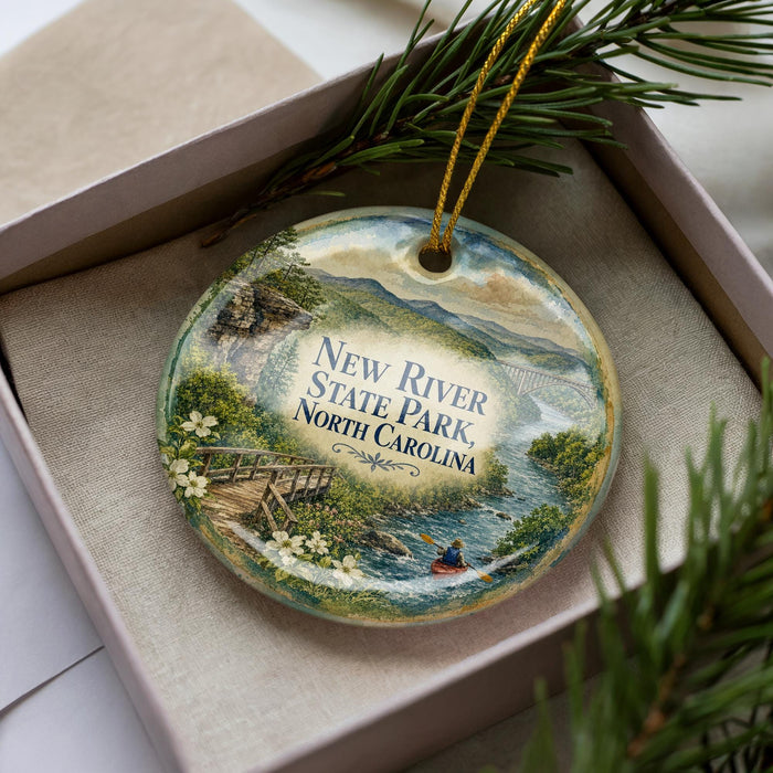 A decorative ornament featuring a scenic landscape with a river, bridge, and mountains, along with a person kayaking, is displayed in a box.