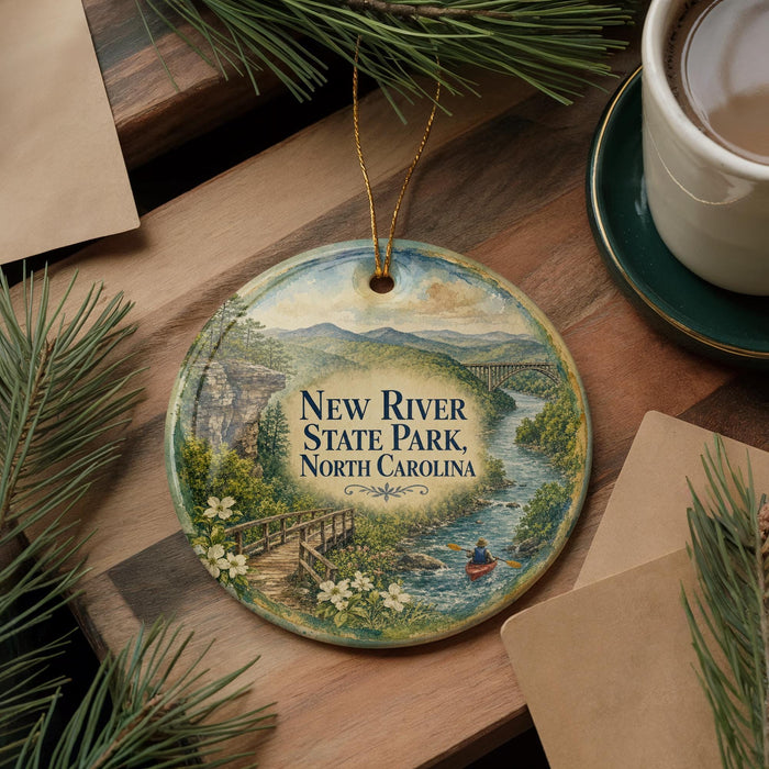 A decorative ornament featuring a scenic landscape of New River State Park in North Carolina, with a small boat on a river and a bridge in the background.