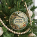 A round ornament hanging on a Christmas tree, featuring a scenic landscape with a lake and mountains.