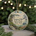A round ornament with a painting of Niagara Falls, a waterfall, and a boat, hanging in front of a Christmas tree with lights.