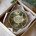 A decorative ornament in a white box, featuring a scenic landscape with a waterfall, a house, and trees.