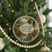 A round ornament hanging on a Christmas tree, featuring a scenic landscape with a waterfall and a cabin.