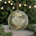 A round ornament with a lighthouse and a bench, surrounded by greenery and a blurred background of trees and lights.