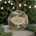 A round ornament with a painting of a historical park scene, featuring a church, palm trees, and a river, hanging in front of a Christmas tree with lights.