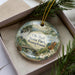 A decorative ornament with a scenic landscape of Ole Bull State Park, Pennsylvania, featuring a bridge, pine trees, and a river.