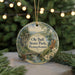 A decorative ornament featuring a scenic landscape with a bridge, pine trees, and a river, hanging from a string.