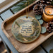 A wooden tray with a decorative ornament featuring a scenic landscape of Oliver Lee Memorial State Park, New Mexico, and pine cones.