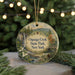A round ornament with a scenic image of a waterfall and forest, surrounded by greenery, is displayed in front of a Christmas tree with twinkling lights.