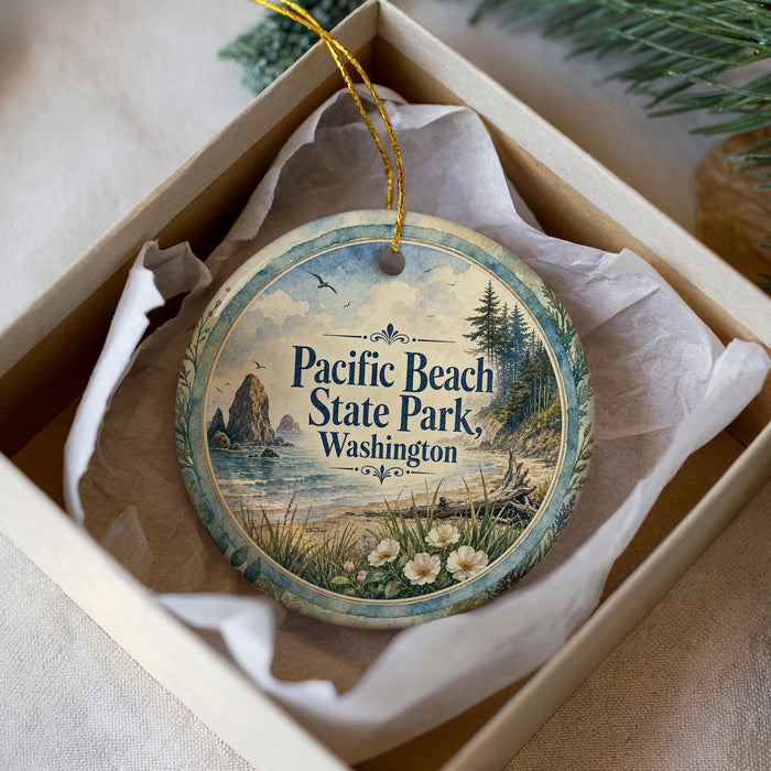 A decorative ornament in a white box, featuring a scenic image of Pacific Beach State Park in Washington with a pine tree and a body of water.