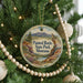 A round ornament hanging on a Christmas tree, featuring a scenic landscape with mountains and a river.