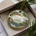 A decorative ornament in a box, featuring a scenic landscape with a waterfall and mountains, along with the text "Palisades State Park, South Dakota".