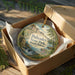 A decorative ornament in a box, featuring a scenic landscape with a waterfall and mountains, with the text "Palisades State Park, South Dakota" prominently displayed.